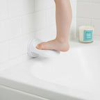 Person using a white non-slip mat on a bathtub ledge with a candle in the background.