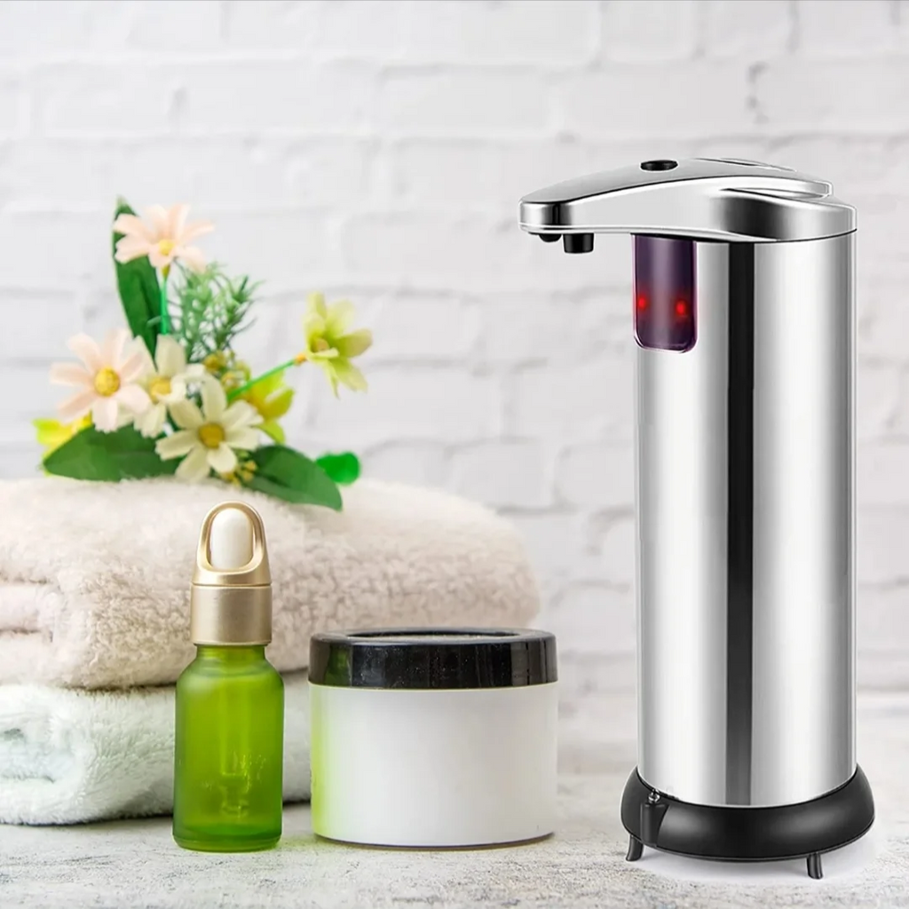 Silver soap dispenser next to a green bottle and white jar on a light wooden surface with a white brick wall background.