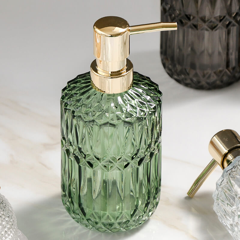 Green glass soap dispenser with gold pump on a light surface