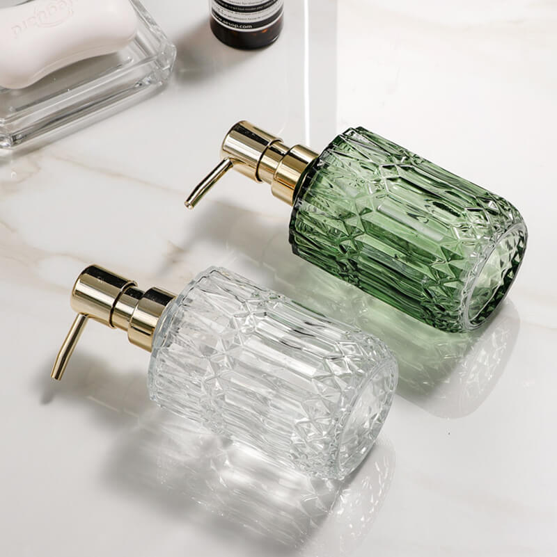 Two glass soap dispensers with gold pumps on a light surface