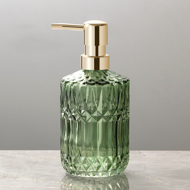 Green glass soap dispenser with gold pump on a gray background
