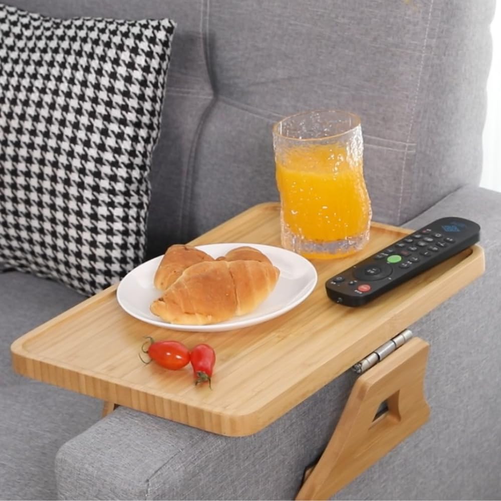 Wooden tray on a couch with croissants, orange juice, and remote control.