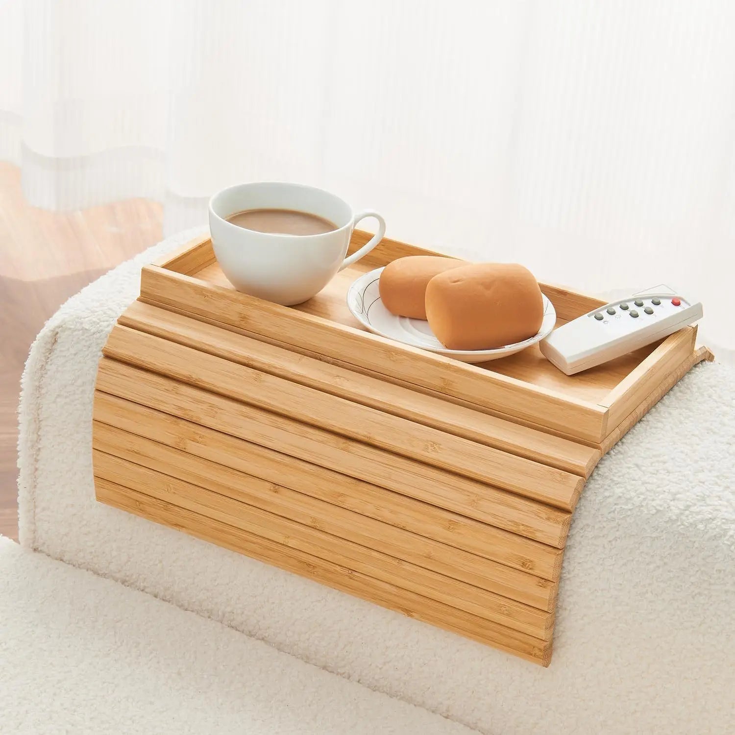 Wooden tray on a sofa with a cup of coffee, bread, and remote control.