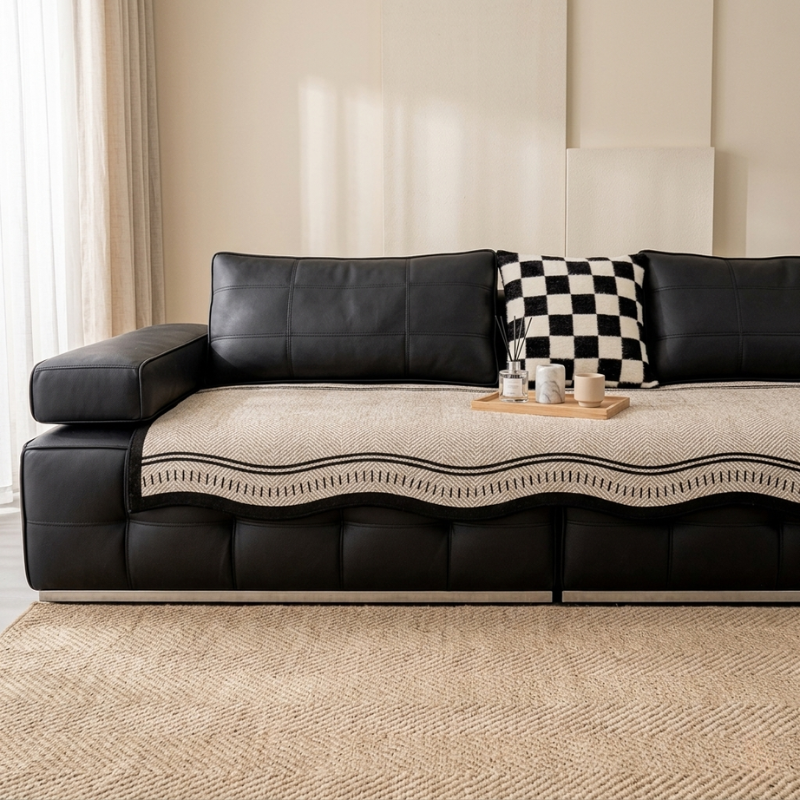 Black leather sectional sofa with a patterned throw blanket and decorative items in a living room.