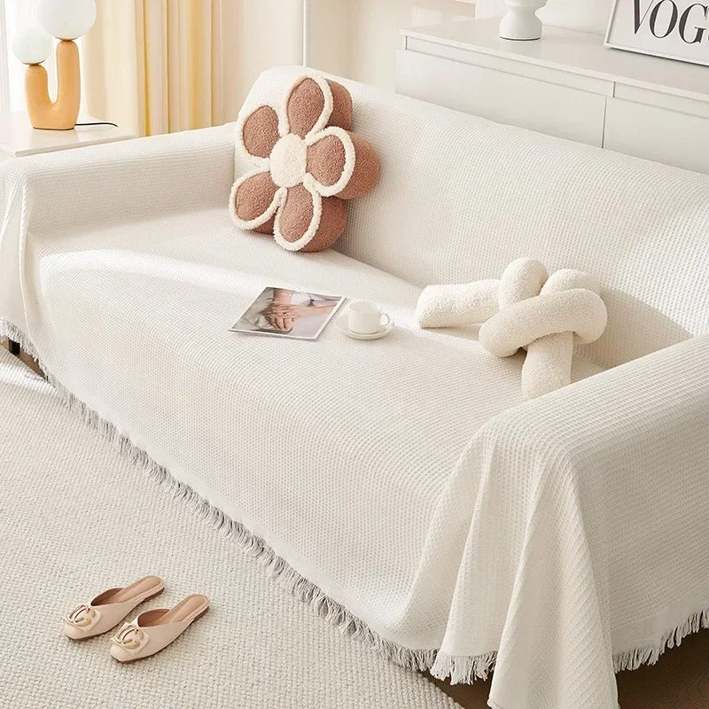 White sofa with decorative pillows and a blanket in a cozy living room setting.