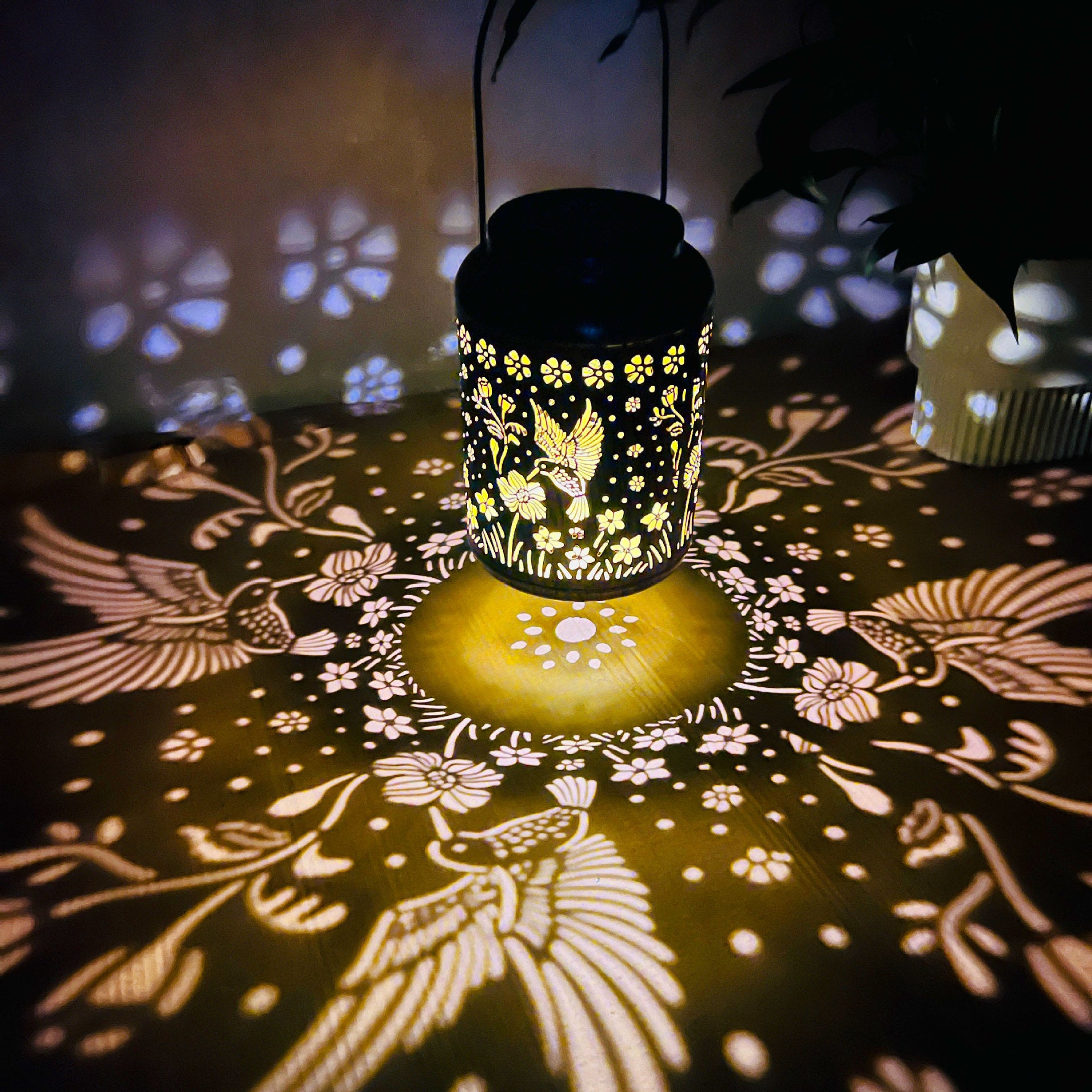Decorative lantern casting bird and floral shadows on a dark surface