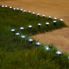 Outdoor solar garden lights arranged along a grassy lawn bordering a tan pathway, casting a cool blue-white glow at night.
