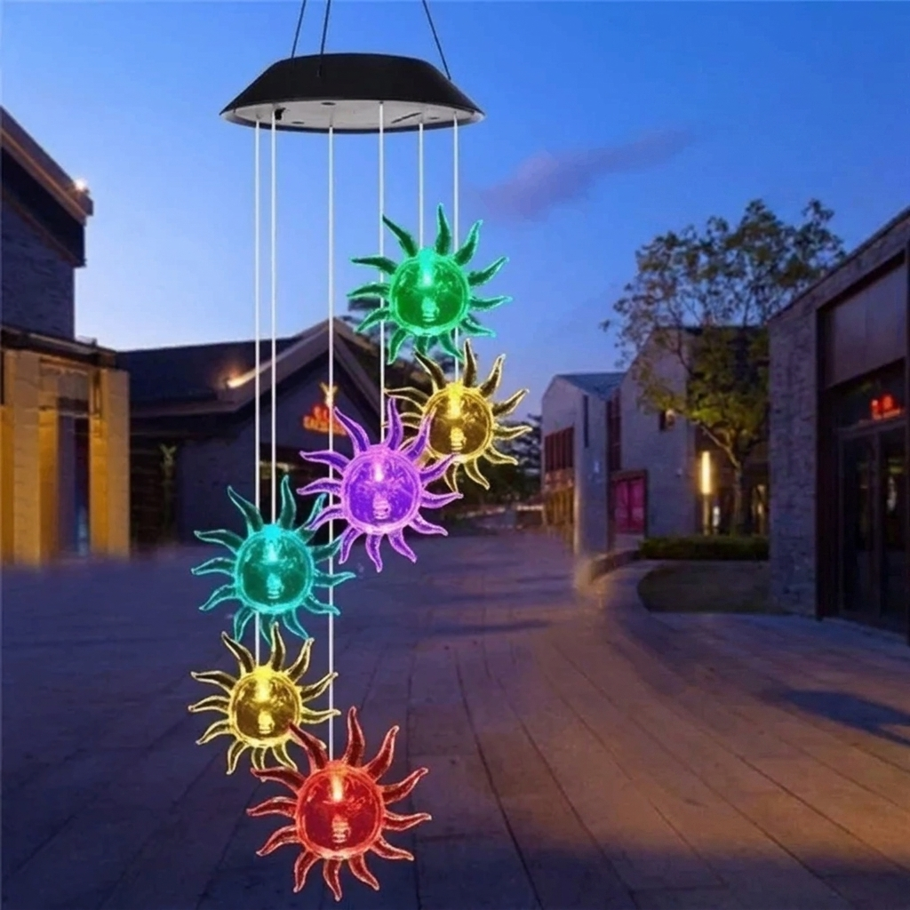 Colorful solar wind chime hanging outdoors with a building and trees in the background.