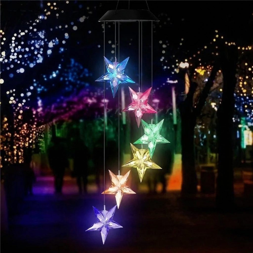 Colorful star-shaped wind chime hanging against a dark background with blurred lights.