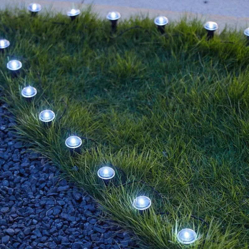 Outdoor solar landscape lights arranged along the edge of green grass and dark gravel, casting a cool white glow.
