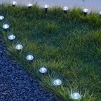 Outdoor solar landscape lights arranged along the edge of green grass and dark gravel, casting a cool white glow.