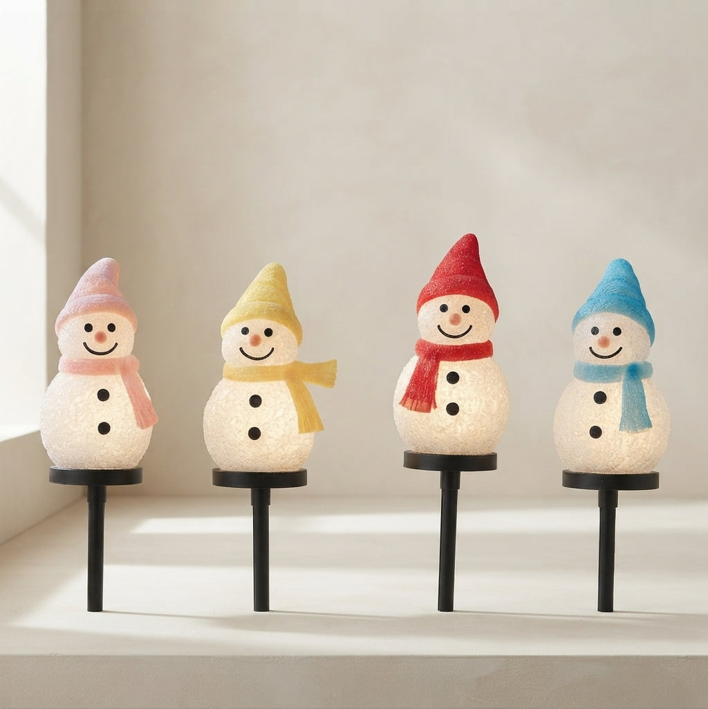 Four snowman-shaped solar garden lights with textured white bodies, each wearing a different colored hat and scarf in pink, yellow, red, and blue, displayed on a light beige surface against a neutral background.