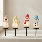 Four snowman-shaped solar garden lights with textured white bodies, each wearing a different colored hat and scarf in pink, yellow, red, and blue, displayed on a light beige surface against a neutral background.