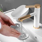Person washing a clear glass under a white and gold faucet.