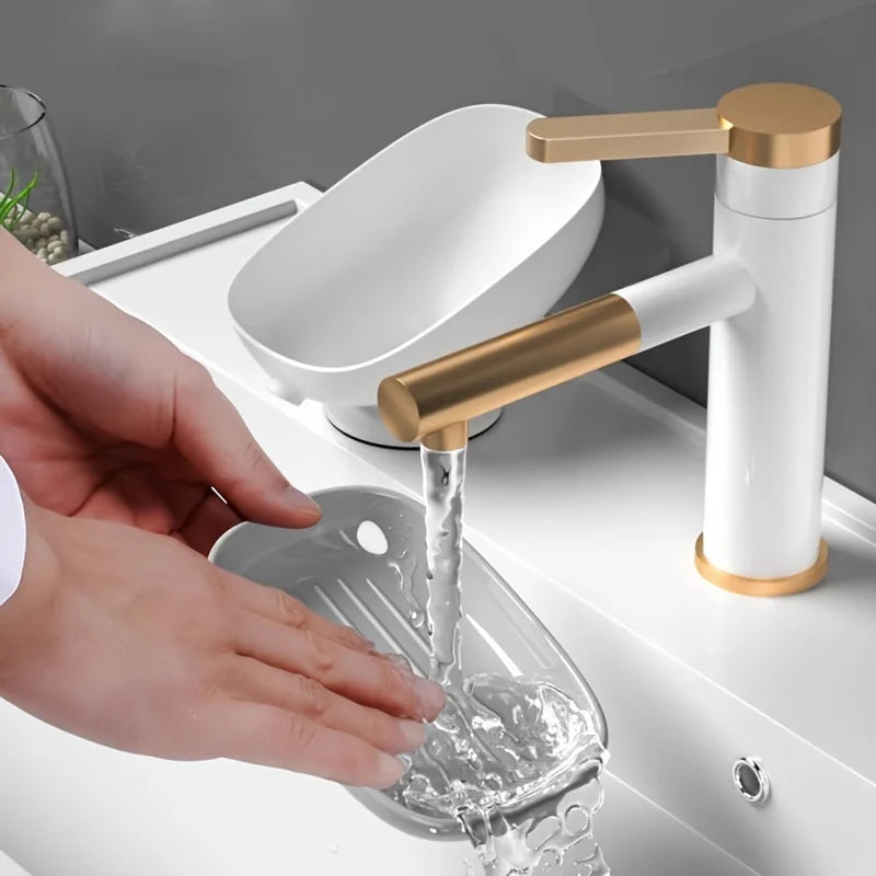 Person washing a clear glass under a white and gold faucet.