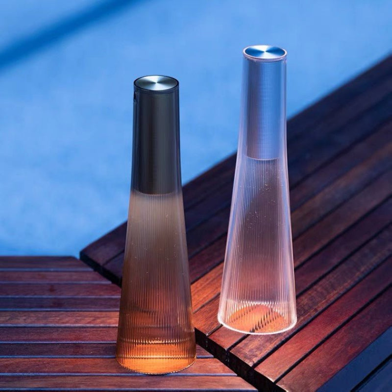 Two tall, cylindrical outdoor lamps on a wooden surface with a blue background