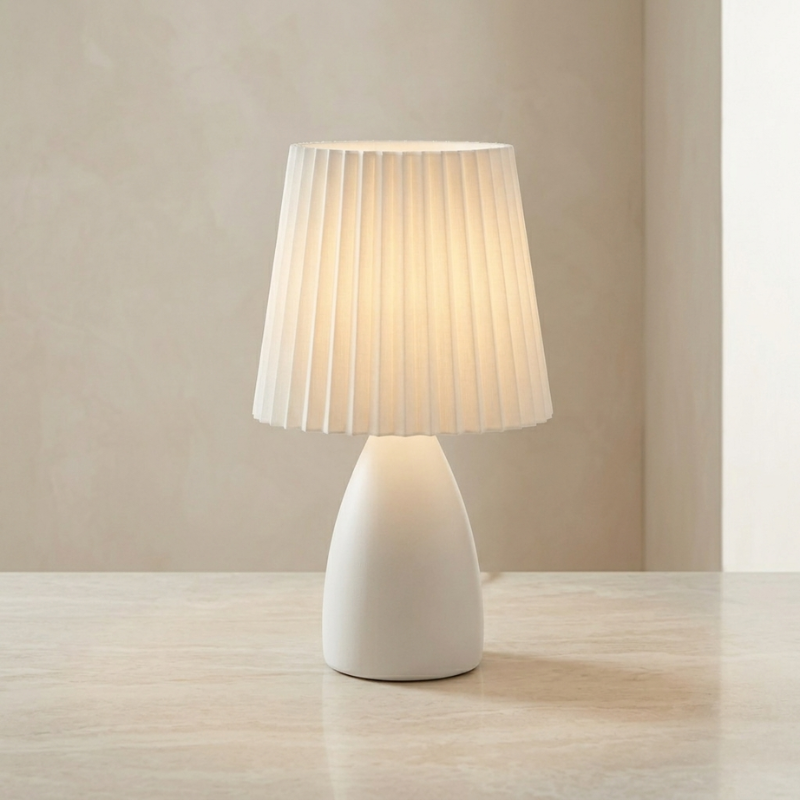 White table lamp with pleated shade on a wooden surface against a beige wall