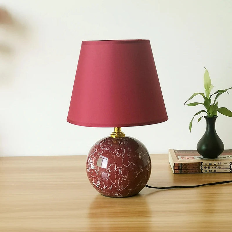 Table lamp with a red shade and marbled base on a wooden surface.