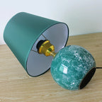 Table lamp with green textured glass bulb and teal fabric shade on a wooden surface.