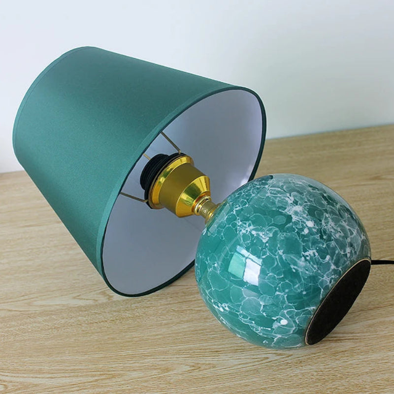 Table lamp with green textured glass bulb and teal fabric shade on a wooden surface.