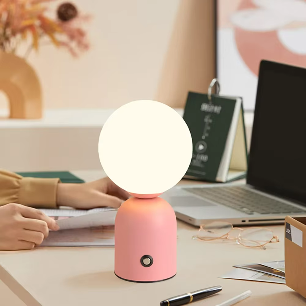 Pink table lamp on a desk with a laptop and books in the background