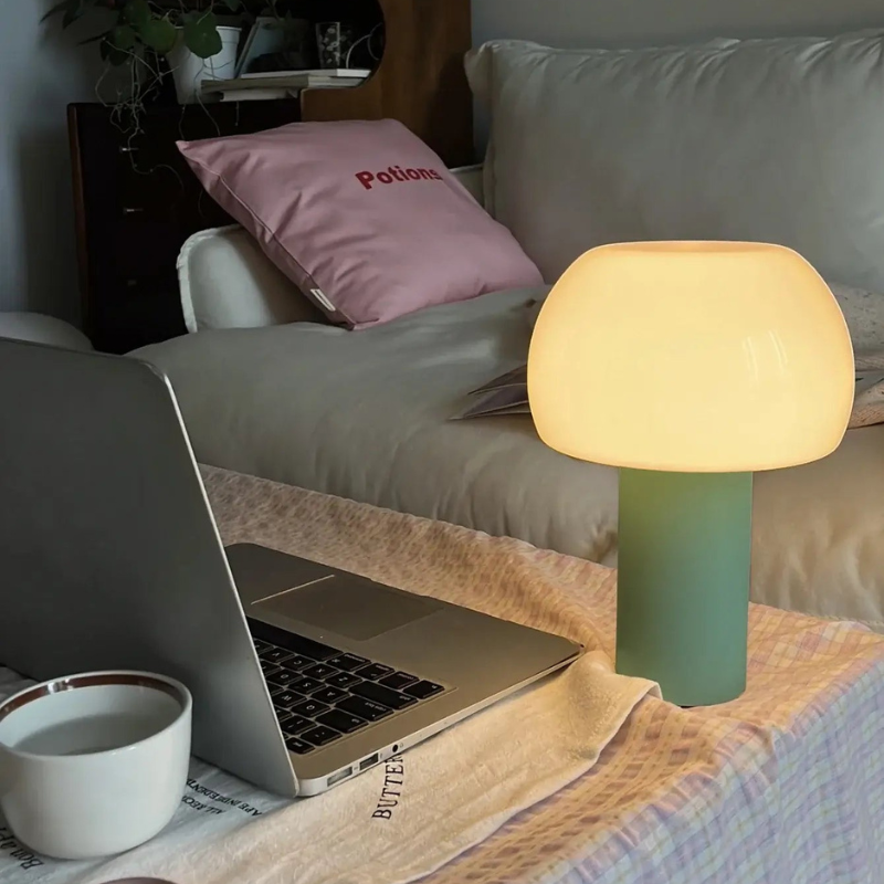 Laptop on a bed with a lamp and cup nearby