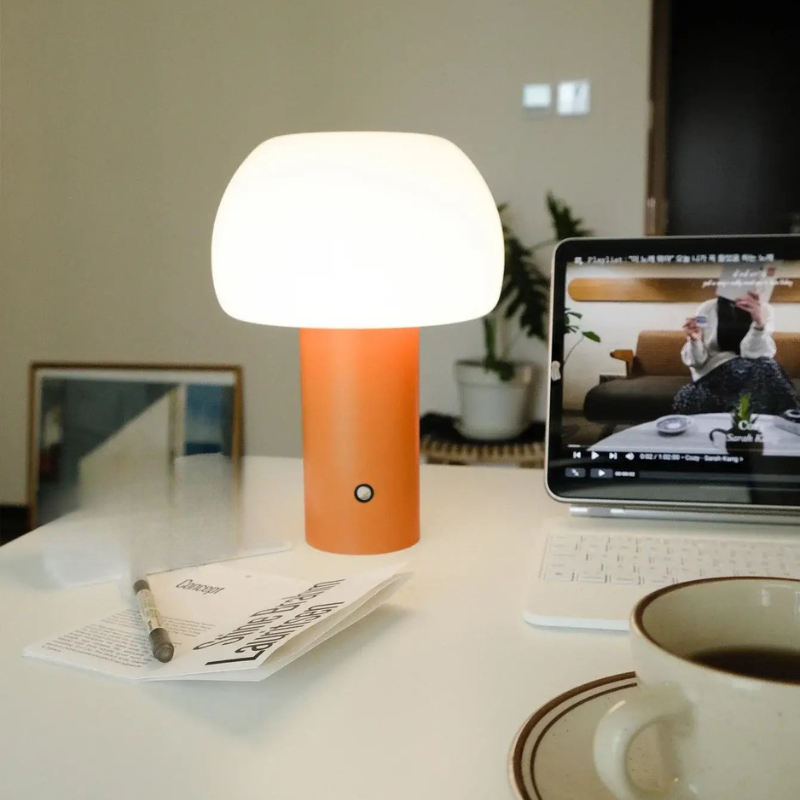 Orange and white lamp on a desk with a laptop and coffee cup in the background