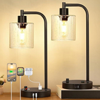 Two black table lamps with glass shades on a wooden surface, with electronic devices charging below.