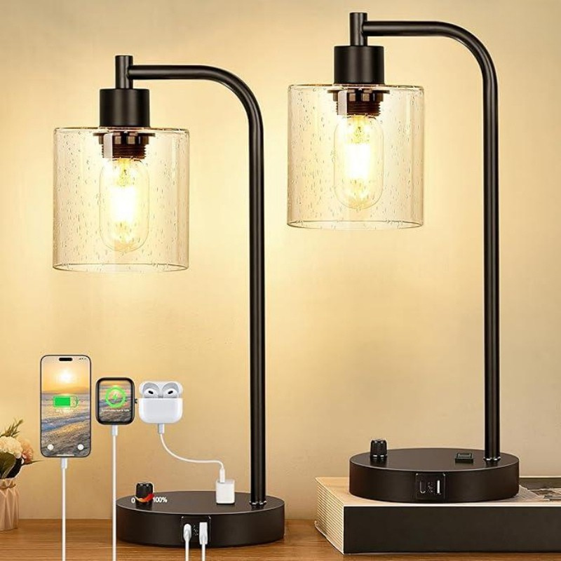 Two black table lamps with glass shades on a wooden surface, with electronic devices charging below.