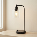 Modern black table lamp with clear glass shade on a wooden surface.