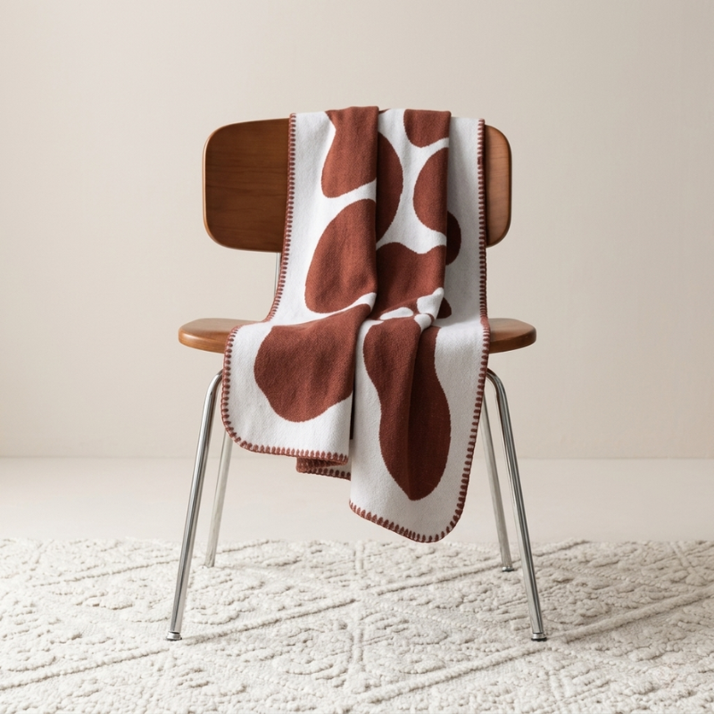 Brown and white patterned blanket draped over a wooden chair on a textured floor.