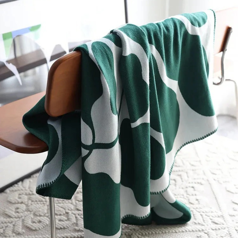 Green and white patterned blanket draped over a wooden chair in a room with a rug.