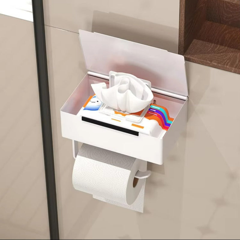 A white wall-mounted tissue holder with a hinged lid and tissue dispenser, shown holding toilet paper and tissues. The image includes promotional text about a silicone switch cover for dust protection.