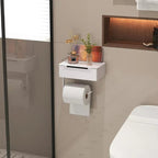 A white wall-mounted toilet paper holder shelf with a toilet paper roll attached, installed in a modern bathroom next to a toilet and shower glass.