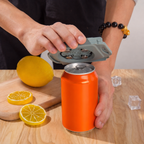 Person using a can opener on an orange can with lemons and ice cubes on a wooden surface.