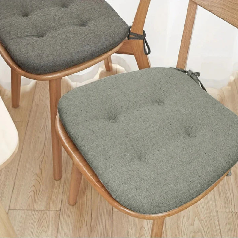 Gray cushioned chair pads on wooden chairs with a light wood floor background.