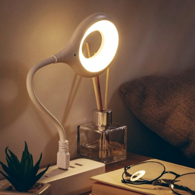 Modern desk lamp with flexible neck on a bedside table next to books and a plant.