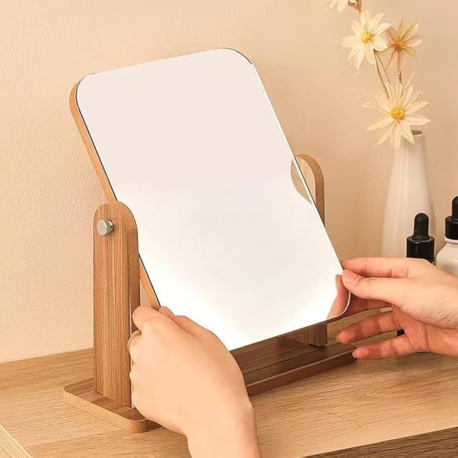 Person using a wooden-framed mirror on a table with a neutral background