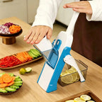 A person using a blue and white manual mandoline slicer on a wooden countertop, with sliced vegetables and lemon slices visible in containers and around the workspace.