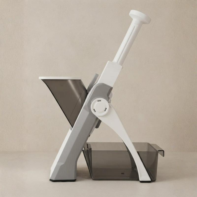 A modern kitchen food chopper or mandoline-style slicer with a white handle, gray plastic frame, and dark translucent tray, shown on a plain beige studio background.