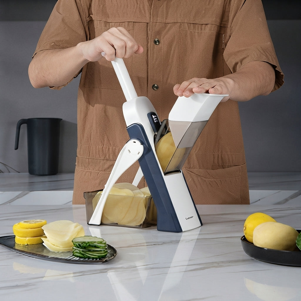 A person in a brown shirt uses a white and navy manual slicer/chopper to cut a potato on a marble countertop, with sliced vegetables and lemons arranged nearby.
