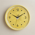 A round wall clock with a yellow lemon slice design on the face and a matching yellow rim, shown against a plain light beige wall.