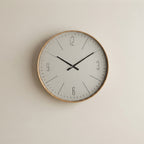 A minimalist round wall clock with a light wood frame, white face, and black hands, mounted on a plain beige wall.