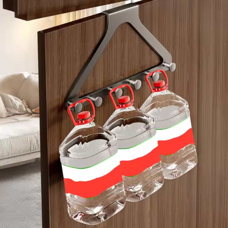 A dark gray over-the-door hanging organizer with three hooks holding three clear plastic water jugs with red caps, shown in a home setting with a wooden door and a sofa in the background.