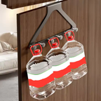 A dark gray over-the-door hanging organizer with three hooks holding three clear plastic water jugs with red caps, shown in a home setting with a wooden door and a sofa in the background.