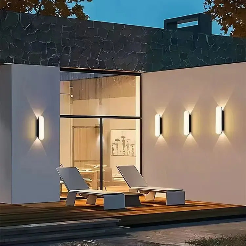 Modern outdoor setting with lounge chairs and wall lights on a house exterior.