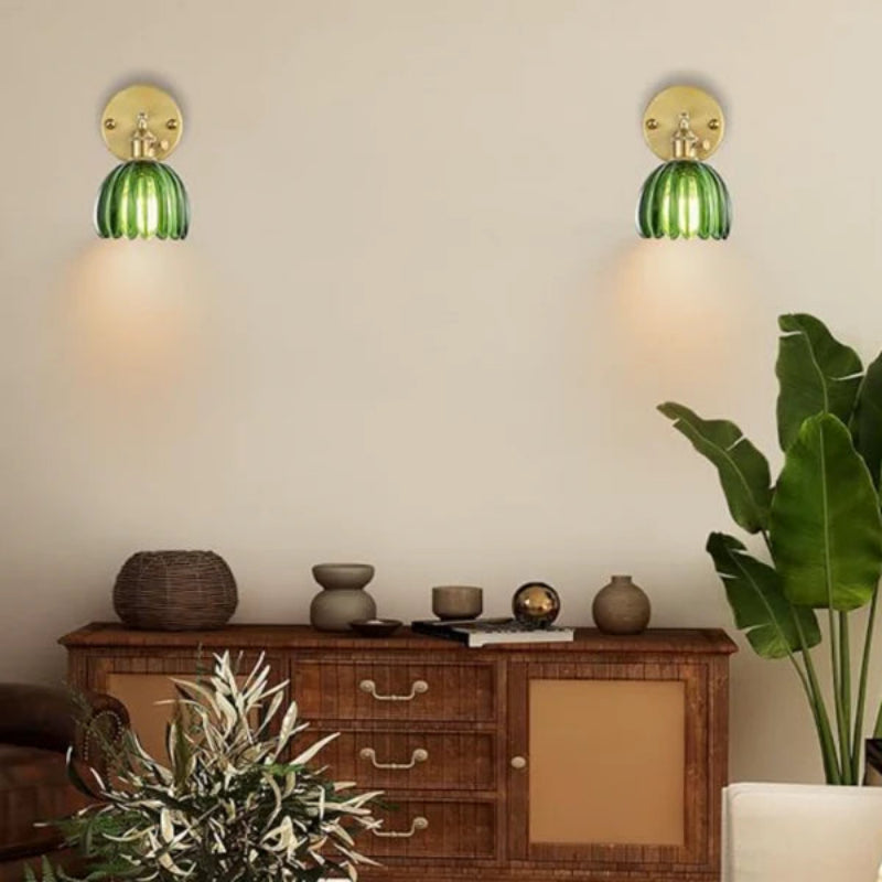 Two green wall sconces on a beige wall above a wooden cabinet with decorative items.