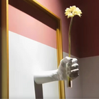 Hand in a white glove holding a yellow flower against a colorful wall.
