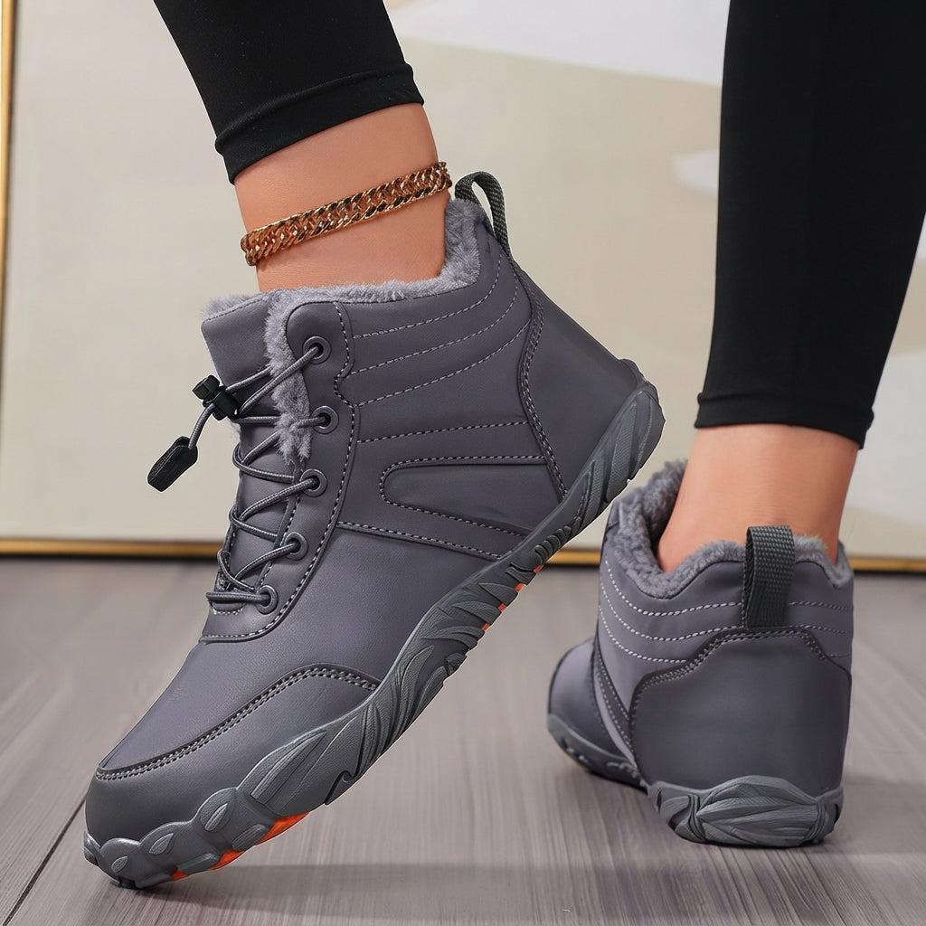 A pair of gray mid-calf winter boots with gray laces and a soft gray faux-fur lining, shown on a person's feet against a neutral indoor background.