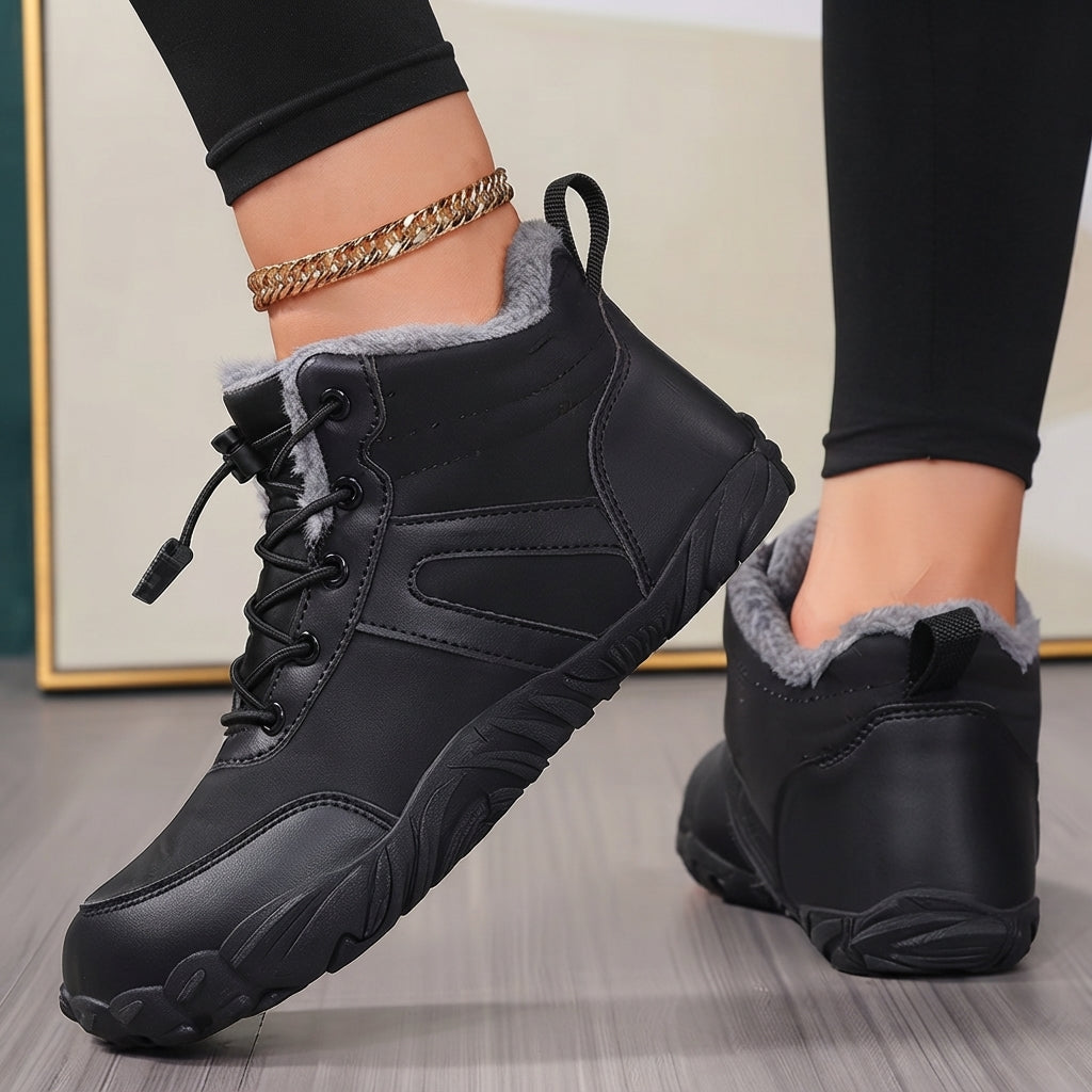 A pair of women's black winter lace-up boots with gray faux-fur lining, shown on a model's feet against a neutral indoor background.